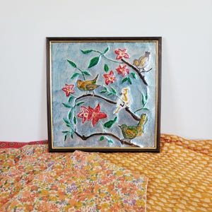 May include: Square framed artwork featuring a textured blue background with embossed birds, red flowers, and green leaves. The birds are in shades of yellow, green, and white. The frame is dark brown.