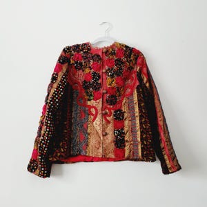 May include: A red, black and gold embroidered jacket with a button fastening. The jacket is made from a variety of fabrics and has a patchwork design.