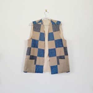 May include: A sleeveless vest with a checkered pattern in shades of brown and blue. The vest has two pockets on the bottom.