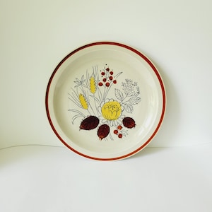 May include: A white ceramic dinner plate with a brown rim and a floral design in shades of yellow, brown, and red.