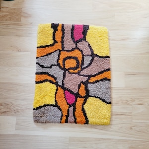 May include: A colorful abstract rug with geometric shapes in shades of yellow, orange, brown, pink, and black.