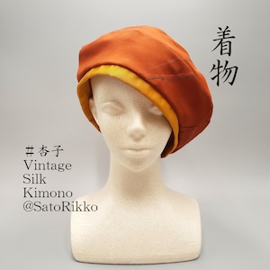 Puede incluir: Un boina naranja con un borde amarillo se muestra en una cabeza de maniquí. La boina es de seda y tiene el texto "Vintage Silk Kimono" y caracteres japoneses.