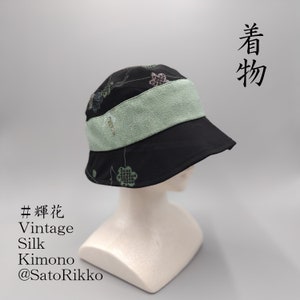 May include: Black bucket hat with a light green band and floral pattern. The hat is made from vintage silk kimono fabric. Text on the hat reads "#輝花 Vintage Silk Kimono @SatoRikko" and Japanese characters.