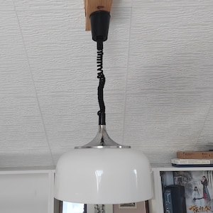 Könnte beinhalten: Eine weiße Deckenleuchte mit einem verchromten Sockel und einem schwarzen Kabel, das von einem Holzbalken hängt.