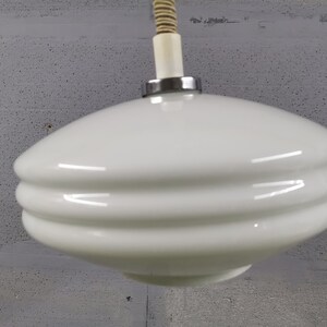 May include: White glass pendant light fixture with a rounded, layered design. The fixture has a chrome finish and a white cord.