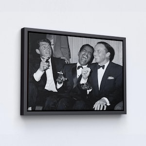 May include: Black and white framed print featuring three men in tuxedos, laughing and smoking. The image captures a candid moment, with one man holding a cigarette and another with a bow tie. The artwork is mounted in a black frame.