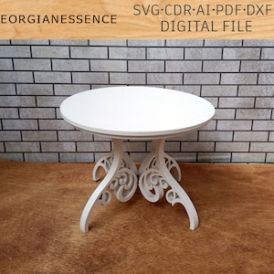 May include: White table with a round top and intricate, carved legs. The table is on a wood floor with a brick wall in the background.