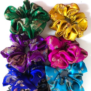 May include: Eight colorful satin scrunchies with a gold dragon pattern. The scrunchies are in the colors green, yellow, purple, pink, blue, turquoise, black, and red.