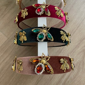May include: Four velvet headbands with gold bee embellishments and colorful rhinestones. The headbands are in shades of beige, burgundy, green, and brown.