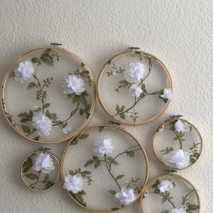 May include: Five embroidery hoops of varying sizes with white fabric and floral designs. The fabric is sheer and the flowers are 3D.
