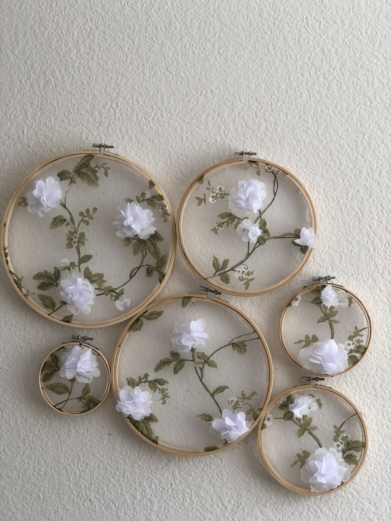 May include: Five embroidery hoops of varying sizes with white fabric and floral designs. The fabric is sheer and the flowers are 3D.