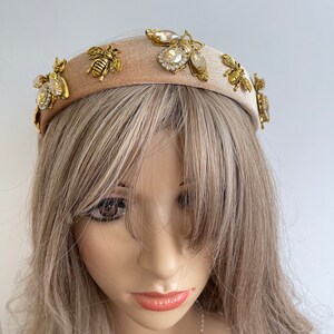May include: A beige velvet headband with gold and clear rhinestone bee embellishments.