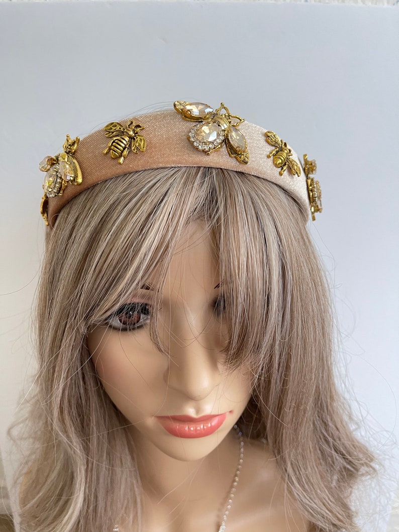 May include: A beige velvet headband with gold and clear rhinestone bee embellishments.
