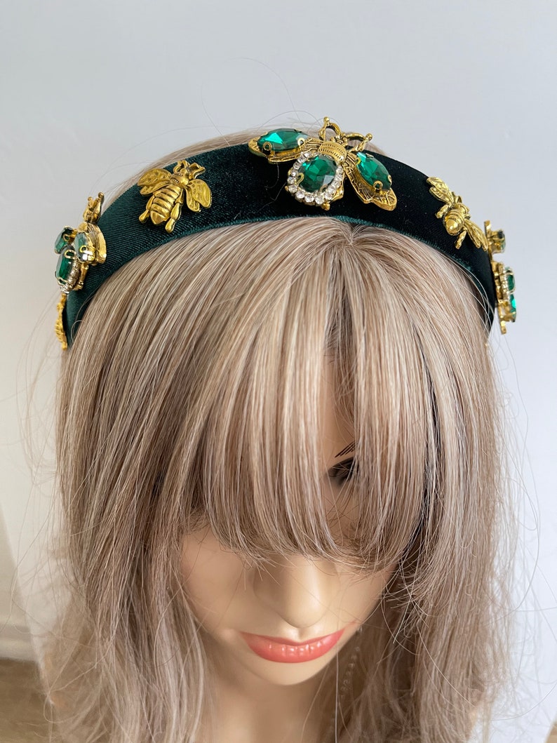 May include: A dark green velvet headband with gold bee and emerald green rhinestone embellishments.