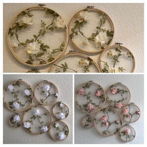 May include: A set of eight embroidery hoops with floral designs. The hoops are made of wood and have a natural finish. The designs are made with white and pink fabric flowers and green leaves.