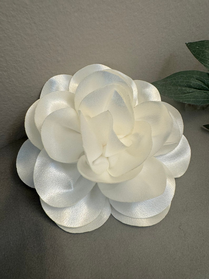 May include: A white satin flower with multiple layers of petals, resembling a camellia.