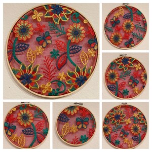May include: Six embroidery hoops with floral designs. The hoops are made of wood and have a pink background with colorful embroidery. The embroidery features flowers, leaves, and butterflies.