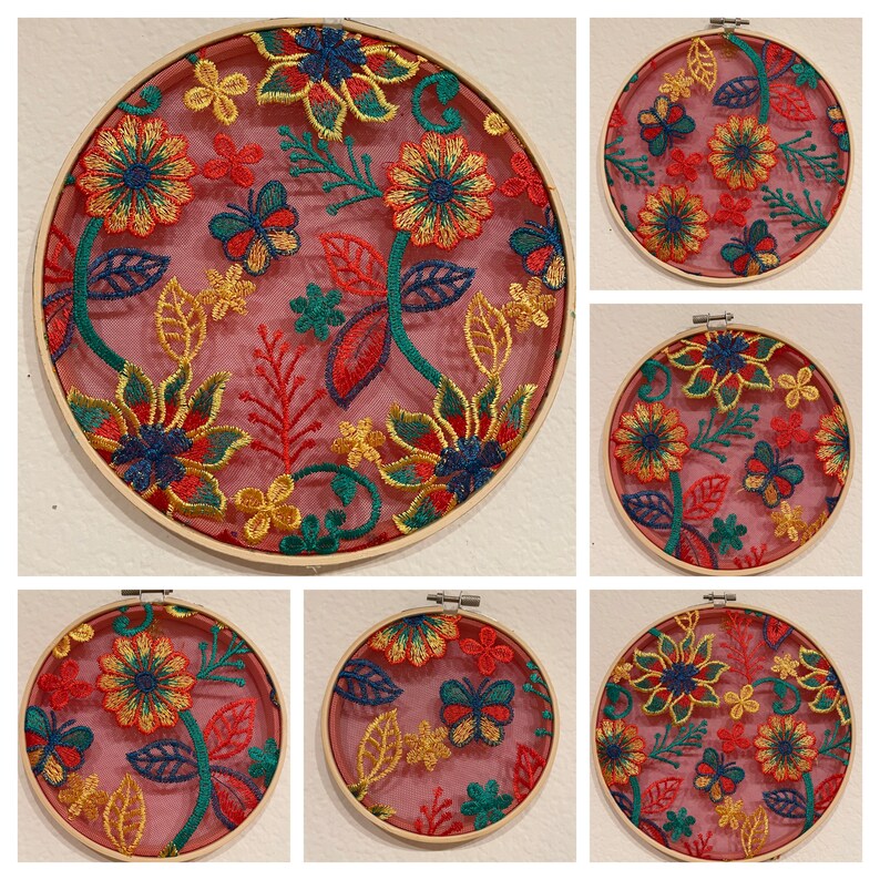 May include: Six embroidery hoops with floral designs. The hoops are made of wood and have a pink background with colorful embroidery. The embroidery features flowers, leaves, and butterflies.