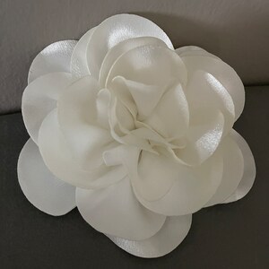 May include: A white satin flower with multiple layers of petals.