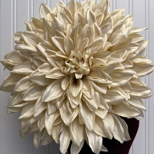 May include: A large, cream-coloured silk flower resembling a dahlia. The flower is made of many petals and has a layered centre.