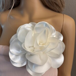 May include: A large white fabric flower with multiple layers of petals. The flower is attached to a pink fabric background.
