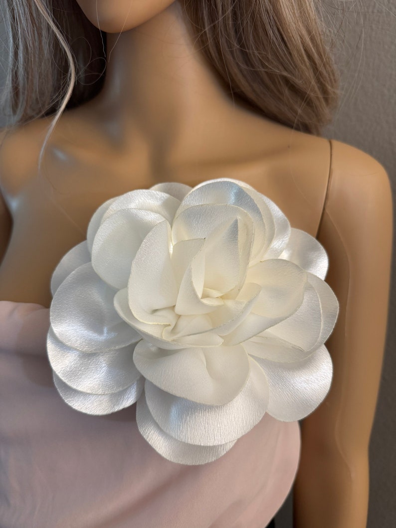 May include: A large white fabric flower with multiple layers of petals. The flower is attached to a pink fabric background.