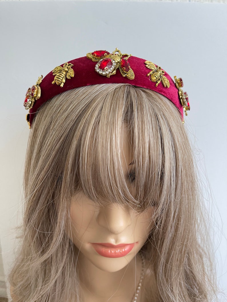 May include: A burgundy velvet headband with gold bee and red rhinestone embellishments.