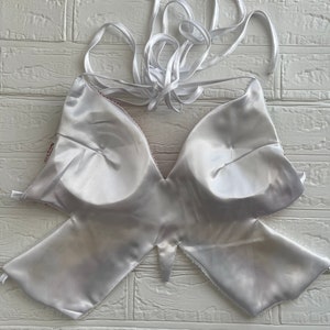 Puede incluir: Top halter blanco de sat&eacute;n con un dise&ntilde;o en forma de mariposa. El top tiene la espalda baja y tirantes ajustables.