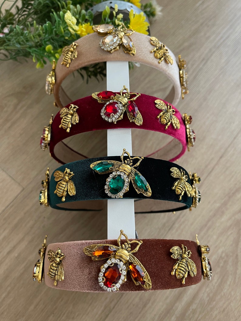 May include: Four velvet headbands with gold bee embellishments and colorful rhinestones. The headbands are in shades of beige, burgundy, green, and brown.