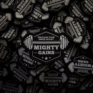 Può includere: Toppa ricamata in bianco e nero con la scritta "MIGHTY GAINS" e un design a bilanciere. La toppa include anche il testo "UNLEASH YOUR INNER BEAST" e "EST. 2018". Le toppe sono sparse su una superficie nera.