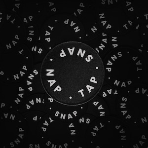 May include: Black circular patches with the words "TAP" and "SNAP" in white, arranged around the edges. The word "NAP" is also present. The patches are scattered on a black background.