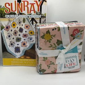 May include: A quilt pattern book titled "Sunray" with a finished size of 74 1/2 inches by 74 1/2 inches. The book is next to a stack of fabric squares with a floral pattern and a tag that says "Day in the Life" by Echo Park.