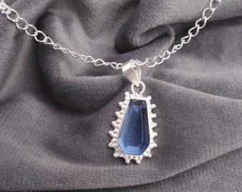 May include: A silver chain necklace with a pendant featuring a dark blue gemstone set in a silver frame with a decorative border.