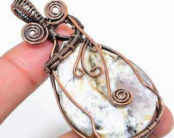 Peut inclure: Un pendentif artisanal avec une pierre en forme de goutte d'eau aux motifs blancs, gris et jaunes. La pierre est sertie dans du fil de cuivre avec des volutes décoratives et une bélière pour une chaîne de collier.