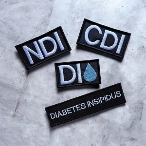 May include: Black embroidered patches with white text. Three rectangular patches read "NDI", "CDI", and "DI" with a blue water droplet. A longer patch reads "DIABETES INSIPIDUS".
