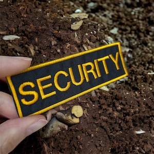 Peut inclure: Un patch noir avec une bordure jaune et le mot "SECURITY" en lettres jaunes.