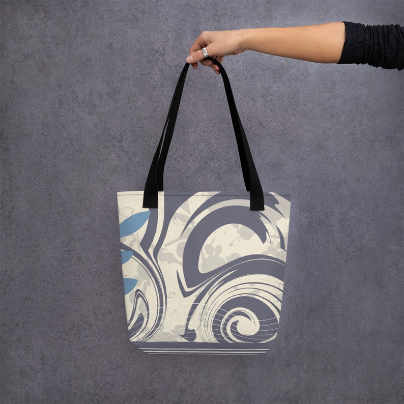 May include: A tote bag featuring a swirling abstract design in shades of grey, white, and blue. The bag has black handles.
