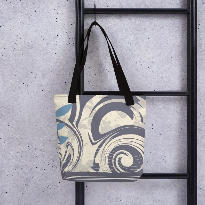 May include: A tote bag with black straps and a cream and grey abstract design. The design features swirls and a blue leaf pattern.