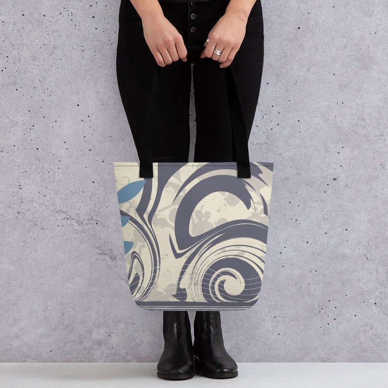 May include: A tote bag featuring a swirling abstract design in shades of blue, grey, and white. The bag has black handles.