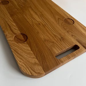 Op de afbeelding: Een groot, ovaalvormig houten snijplank met een handvat en vier ronde uitsparingen. Het plank is gemaakt van lichtbruin hout met een natuurlijke nerf.