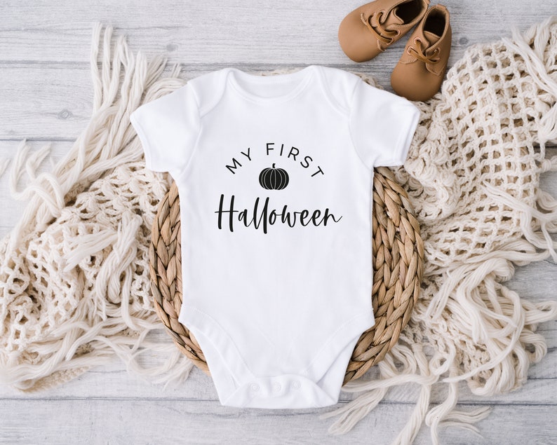 May include: White baby onesie with black text that reads "My First Halloween" and a black pumpkin graphic.