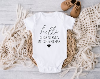 May include: White baby onesie with black text that reads "hello grandma & grandpa" with a small black heart.