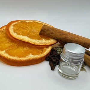 Könnte beinhalten: Getrocknete Orangenscheiben, Zimtstangen, Nelken und ein kleines Glas mit silbernem Deckel. Die Zutaten deuten auf ein Thema der Aromatherapie oder Potpourri hin.