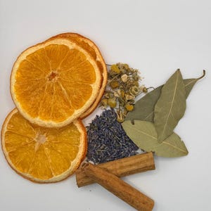 Könnte beinhalten: Eine Sammlung getrockneter Kräuter und Gewürze, darunter Orangenscheiben, Kamillenblüten, Lavendel, Lorbeerblätter und Zimtstangen. Die Orangenscheiben sind leuchtend orange, und die Zimtstangen sind braun.