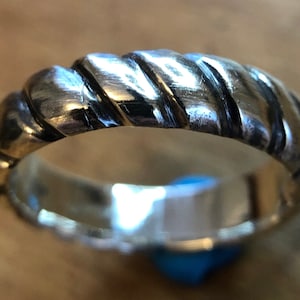 May include: A silver-colored ring with a twisted rope design. The ring has a polished, reflective surface and a detailed texture. The ring is a piece of jewelry, suitable for everyday wear or special occasions.