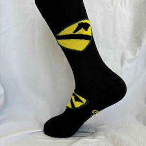 Könnte beinhalten: Schwarze Socken mit einem gelben und grünen Logo auf der Wade. Das Logo ist eine stilisierte Bergkette.