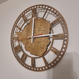 May include: A wooden clock featuring a map of Zimbabwe in the centre. The clock face is surrounded by Roman numerals and a decorative frame.