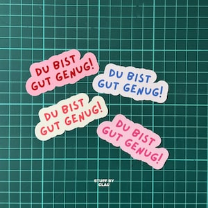 May include: Four die-cut stickers with wavy edges, each featuring the German text "DU BIST GUT GENUG!" in bold, rounded lettering. The stickers come in various colour combinations, including pink with red text, white with blue text, and white with red text.