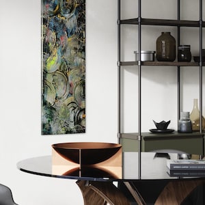 May include: A modern dining room with a glass-top table with a wooden base, a black chair, and a metal shelving unit with a green shelf. A copper bowl sits on the table. A colorful abstract painting hangs on the wall.