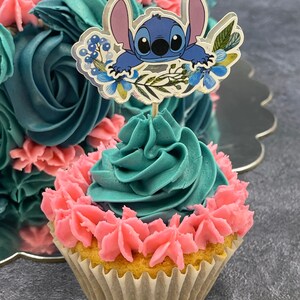 K&ouml;nnte beinhalten: Ein t&uuml;rkisfarbener und rosafarbener Cupcake mit einem blauen Comic-Charakter als Topper. Der Charakter ist Stitch aus dem Disney-Film Lilo & Stitch. Der Cupcake ist mit rosa und t&uuml;rkisfarbenem Frosting verziert.